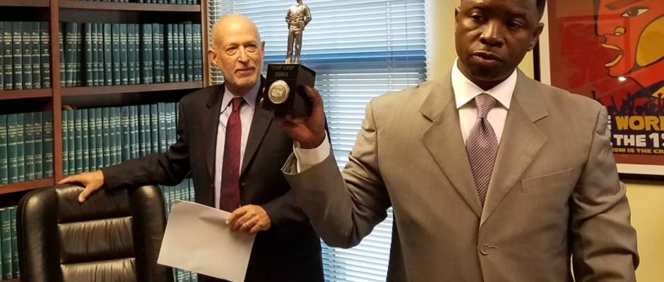 Flanked by his attorney Dan Siegel, Oakland police Sgt. James 'Mike' Gantt holds up an 'officer of the year' award before speaking to reporters about a legal claim he filed against Oakland on Tuesday, Nov. 1, 2016. (Alex Emslie/KQED)